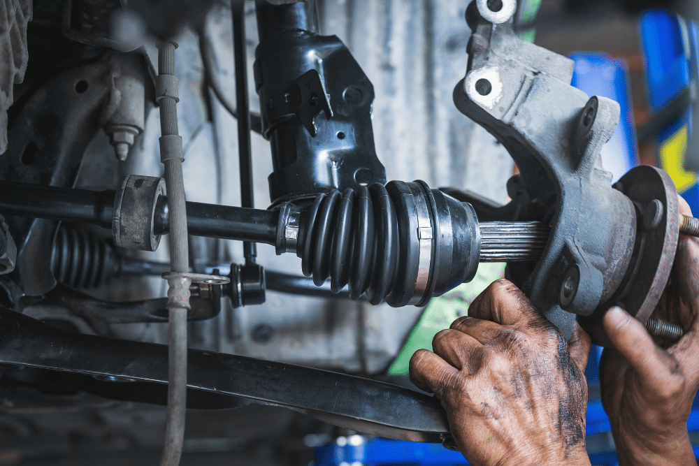 axle replacement, auto repair in Lonsdale, MN at Lonsdale Auto Works. Mechanic installing a new CV axle on a vehicle's suspension system, with hands covered in grease.