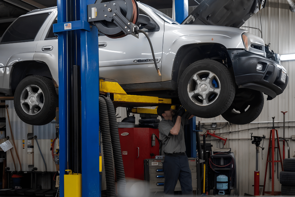 Summer Road Trip Car Prep at Lonsdale Auto Works, Inc. A mechanic inspects underneath a silver vehicle raised on a vehicle lift during a summer road trip maintenance check.